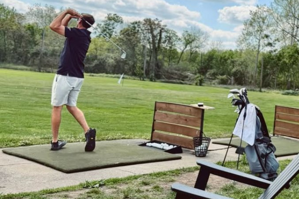 Golfer mid-swing at a driving range bay using QR code ordering for golf courses
