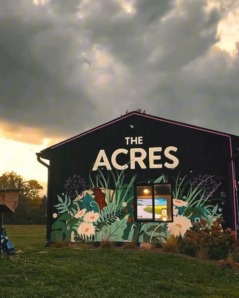 The Acres golf entertainment venue building exterior lit up at sunset